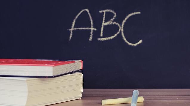 Schulbücher vor einer Tafel in einem Klassenzimmer.