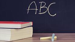 Schulbücher vor einer Tafel in einem Klassenzimmer.