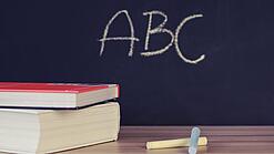 Schulbücher vor einer Tafel in einem Klassenzimmer.