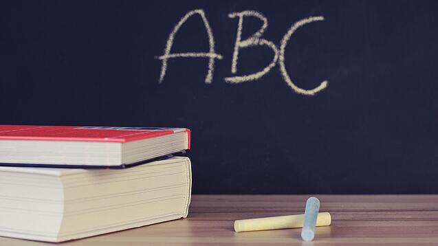 Schulbücher vor einer Tafel in einem Klassenzimmer.