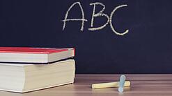 Schulbücher vor einer Tafel in einem Klassenzimmer.