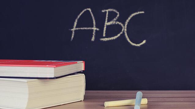 Schulbücher vor einer Tafel in einem Klassenzimmer.