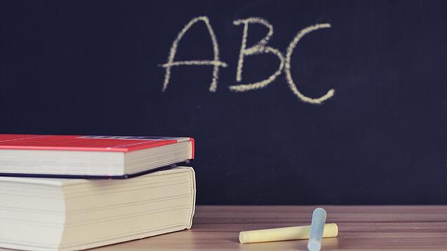 Schulbücher vor einer Tafel in einem Klassenzimmer.