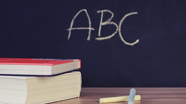 Schulbücher vor einer Tafel in einem Klassenzimmer.