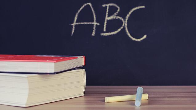 Schulbücher vor einer Tafel in einem Klassenzimmer.