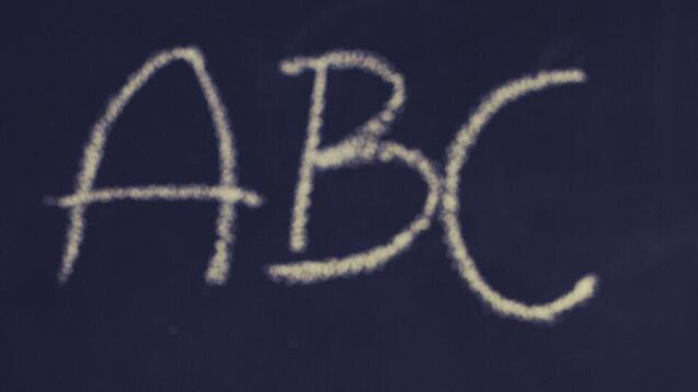 Schulbücher vor einer Tafel in einem Klassenzimmer.