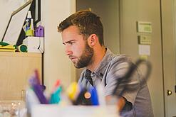 Ein Mann sitzt an einem Schreibtisch und schaut auf einen Computer.