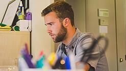 Ein Mann sitzt an einem Schreibtisch und schaut auf einen Computer.