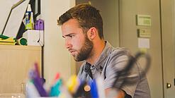 Ein Mann sitzt an einem Schreibtisch und schaut auf einen Computer.