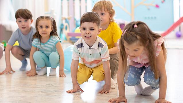 Kleine Kinder hocken auf dem Boden einer Kindertageseinrichtung.