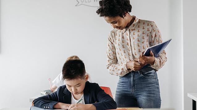 Eine junge Lehrerin beobachtet einen Jungen bei der Erledigung einer Aufgabe.