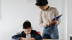 Eine junge Lehrerin beobachtet einen Jungen bei der Erledigung einer Aufgabe.