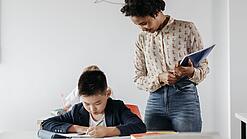Eine junge Lehrerin beobachtet einen Jungen bei der Erledigung einer Aufgabe.