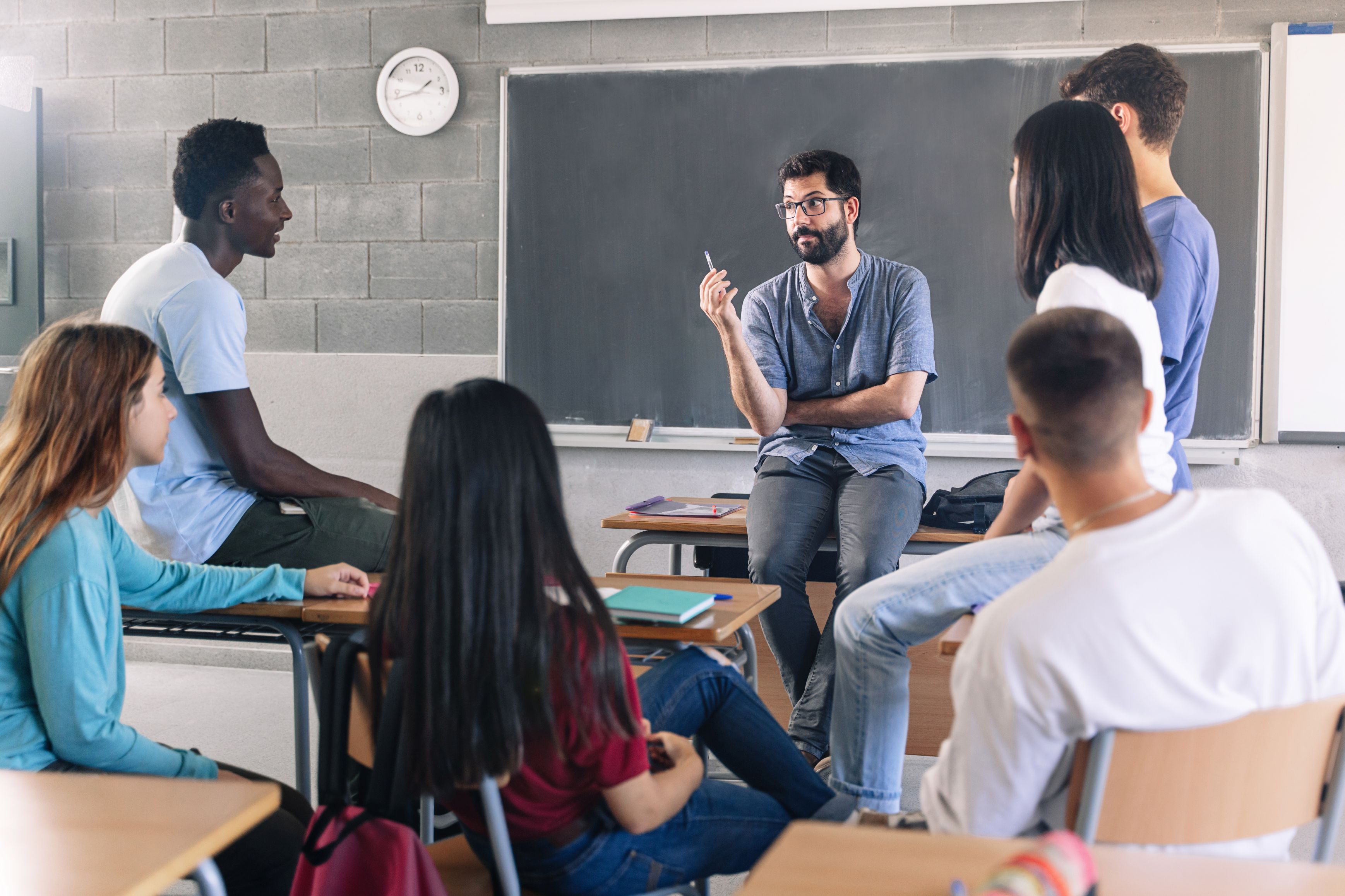 Gruppe diverser Schüler und Schülerinnen sitzt in einem Stuhlkreis und diskutiert mit einem Lehrer
